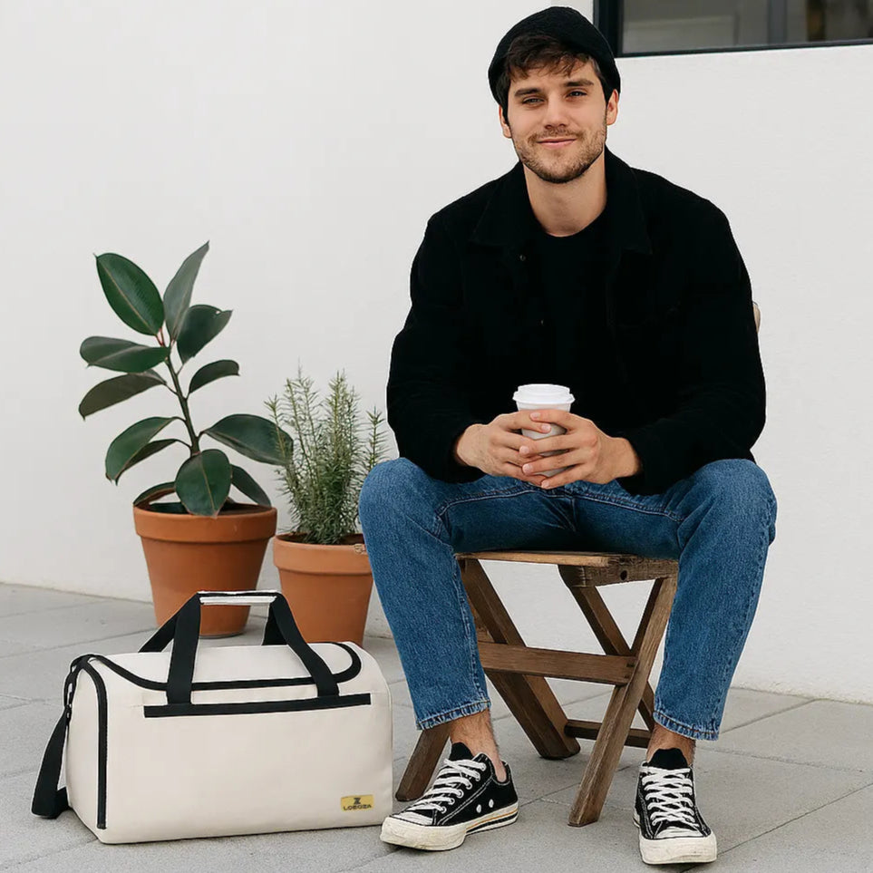 Man sitting on a stool holding a coffee cup with a white bag and plants in the background