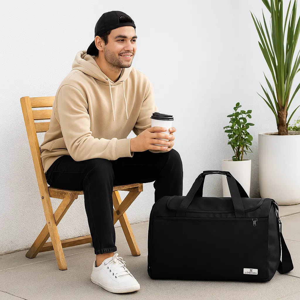 Man sitting on a chair holding a coffee cup next to a black duffel bag in a room with plants.